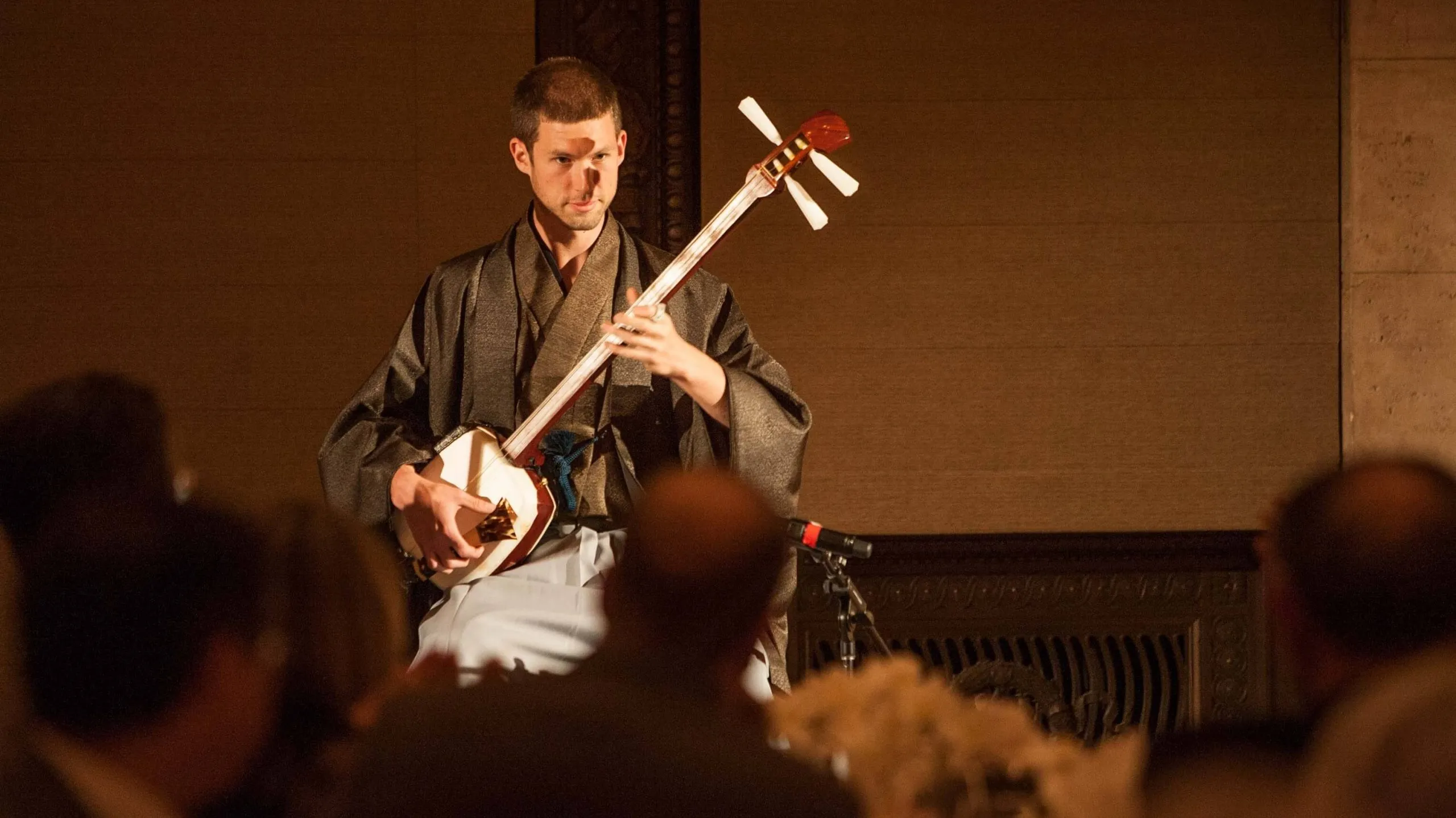 Kyle performing shamisen in a warmly lit hall