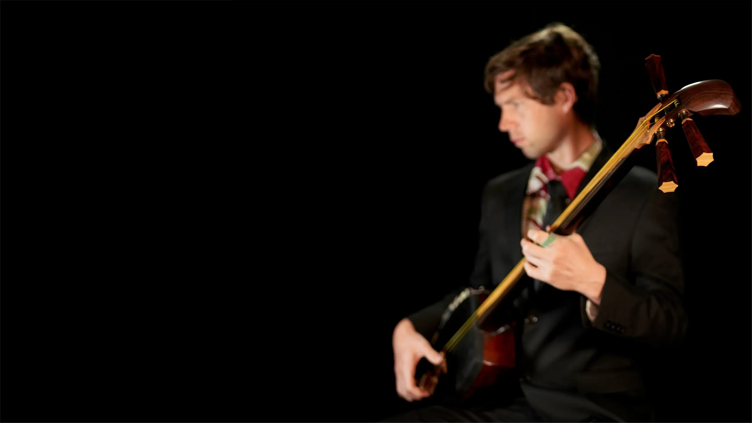 Kyle Abbott playing shamisen, lit against a black background