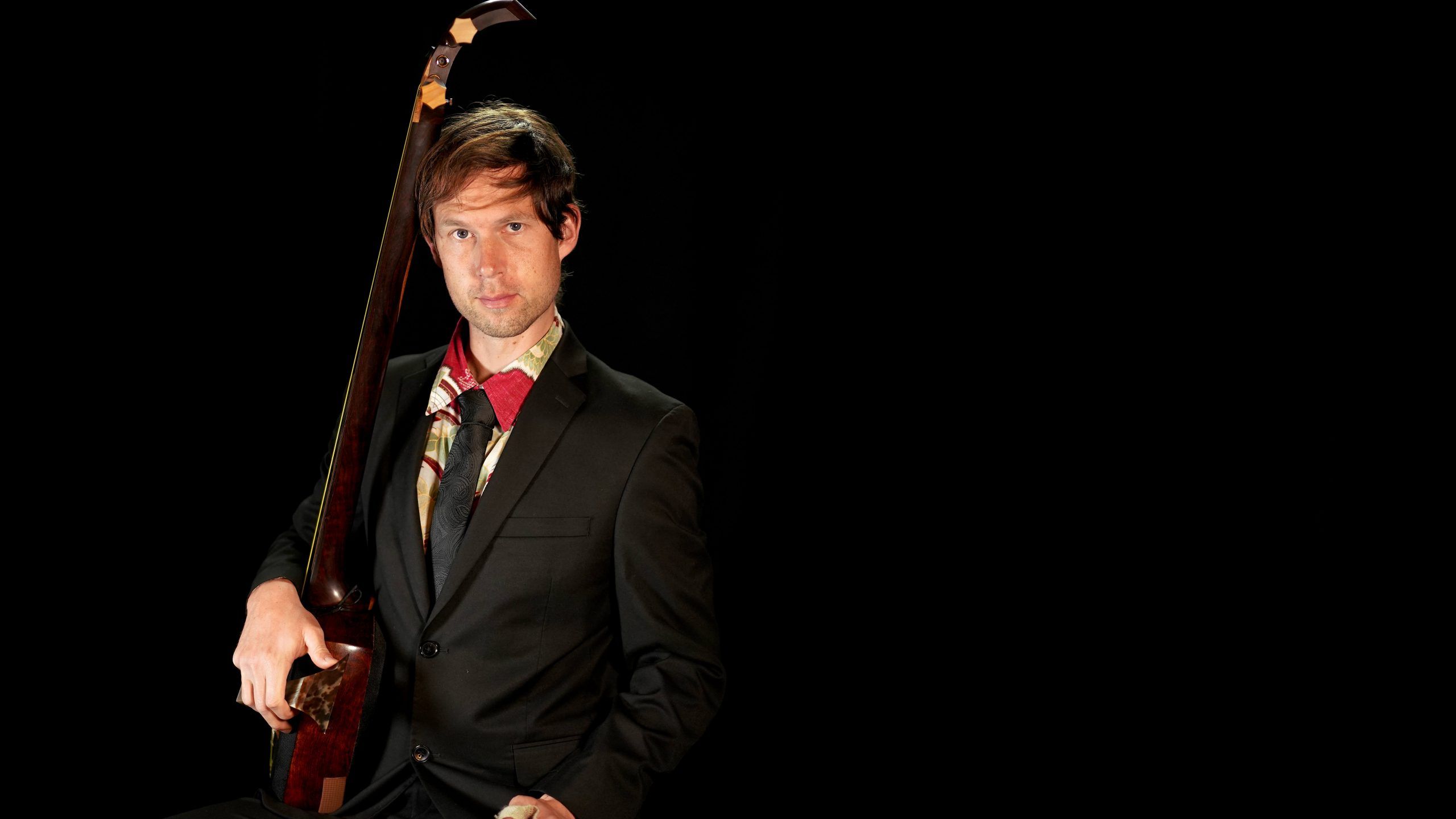 Kyle Abbott in a dark suit holding a Tsugaru shamisen